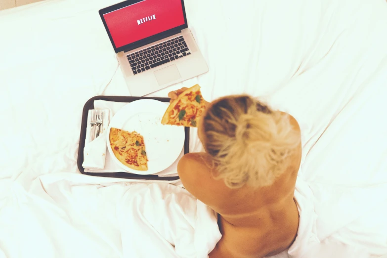 someone taking a pizza and laptop on their bed