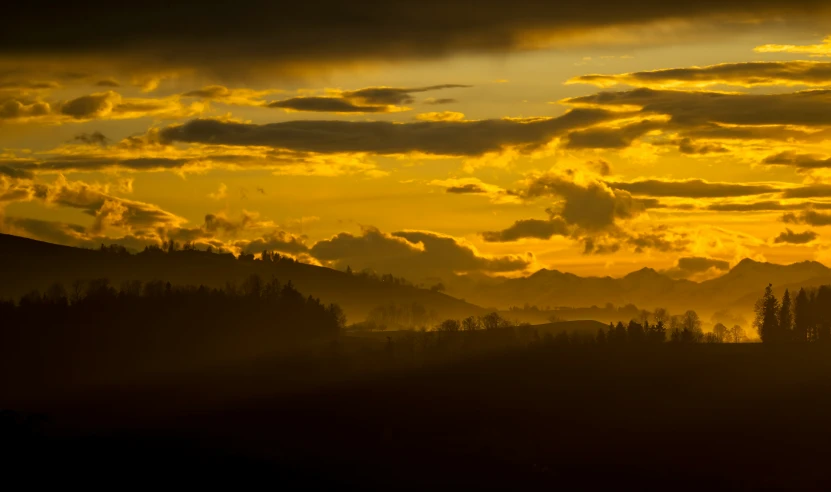 a sun setting over mountains, a mountain range and trees