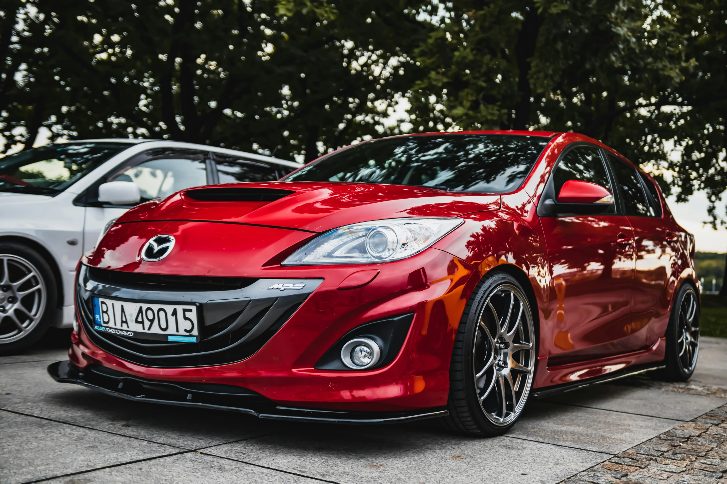 a red mazda car parked next to two silver cars