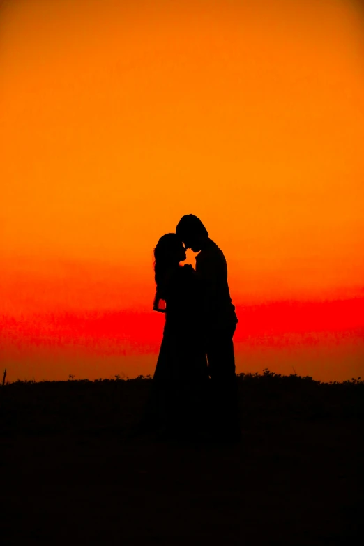 a couple kissing on the beach in silhouette against an orange sky