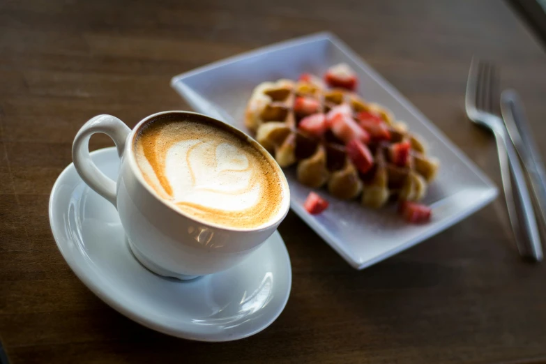 a cup of coffee sitting next to a stack of waffles