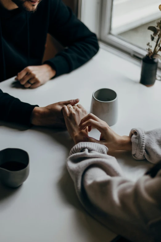 some people are sitting at a table holding hands