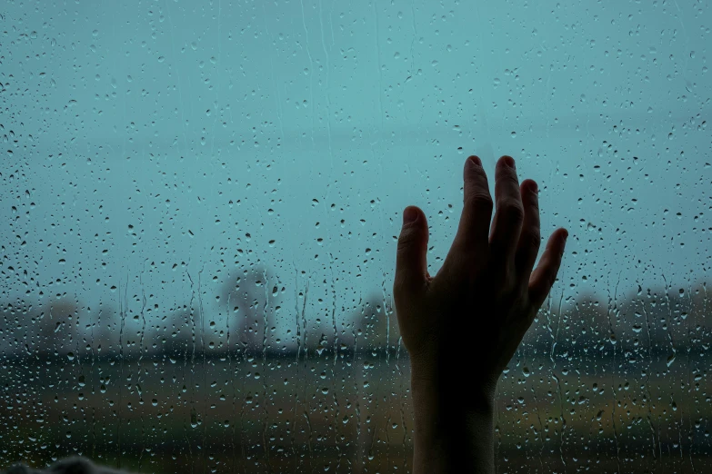 a person's hand up in front of a window with raindrops on it