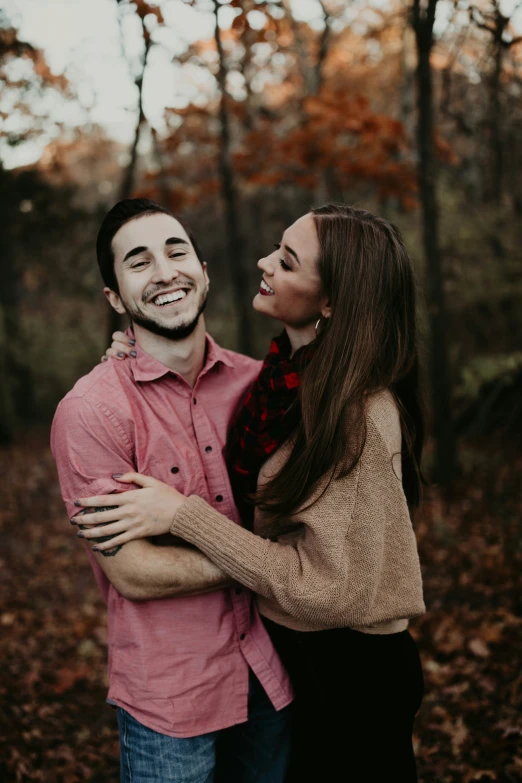 a woman laughs while smiling while hugging a man in the woods