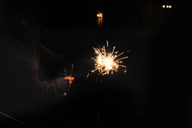 a person holding a glass with fireworks exploding in the night sky