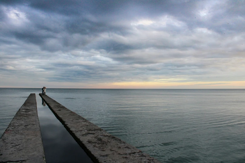 the man is standing on a large stone pier by the water