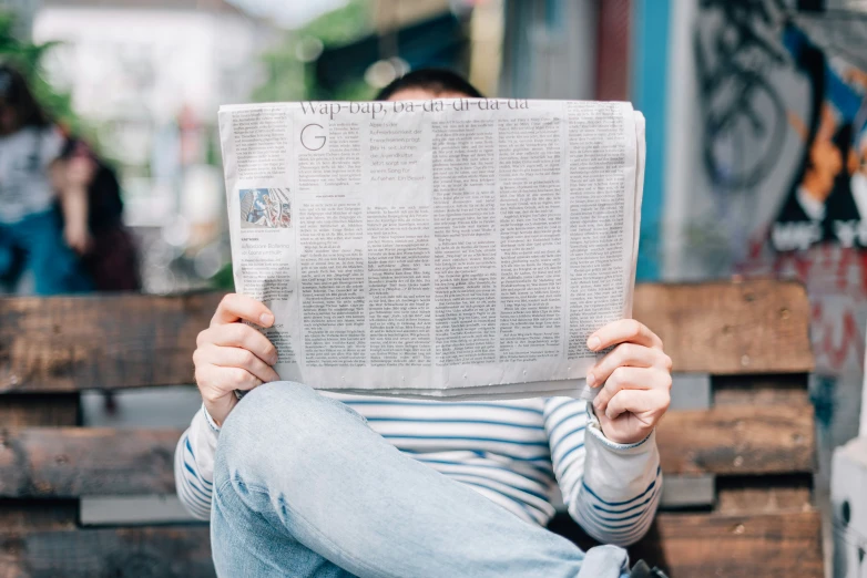 person sitting on the side of a wooden truck with their feet in a newspaper