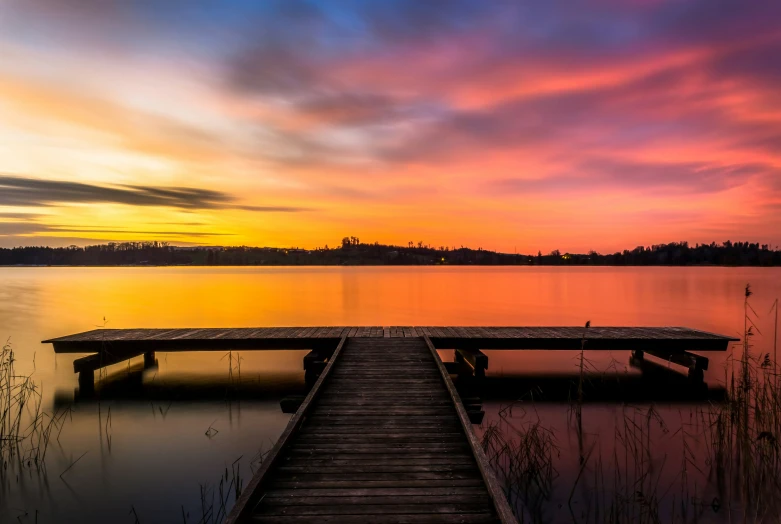 a large body of water with a dock leading into the sunset