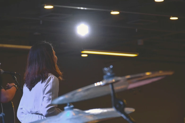 a girl playing the drums on stage in front of a spotlight