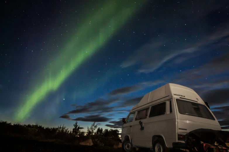 there is an rv under a night sky and there is a bright green aurora