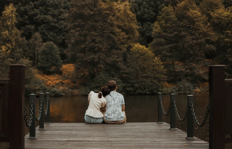 two people are sitting on the bridge as a dog sniffs them