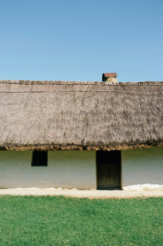 a small thatched roof on an old house with grass in front