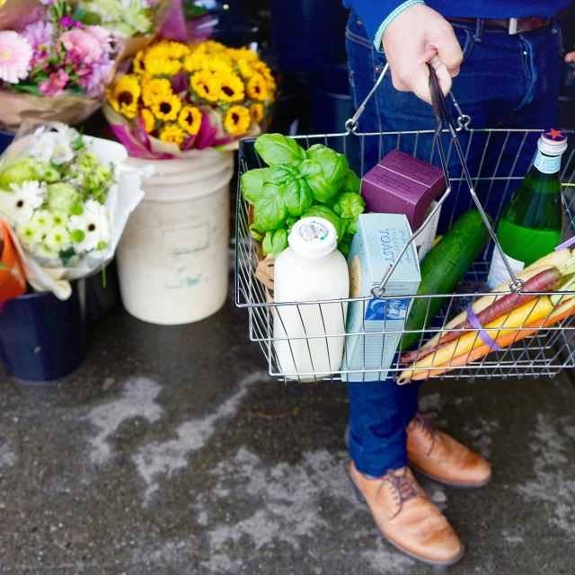 a woman holding a shopping basket full of fresh vegetables