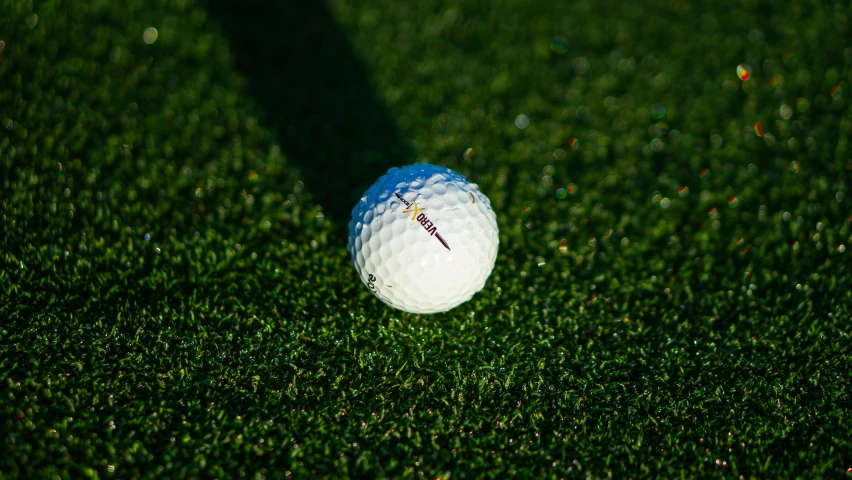 a golf ball on the ground with its shadow cast by the grass