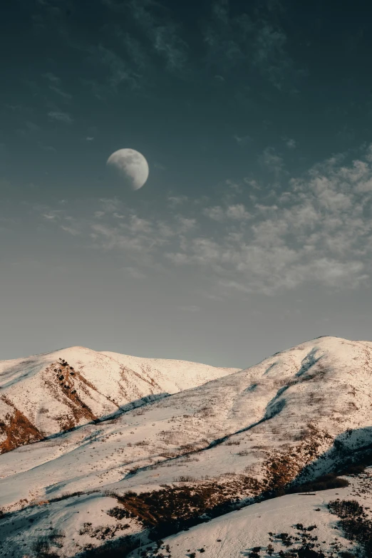 a snowy mountain area with a moon in the distance