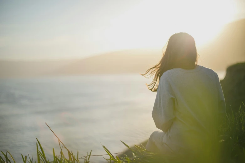 a person sitting on grass facing water on a sunny day