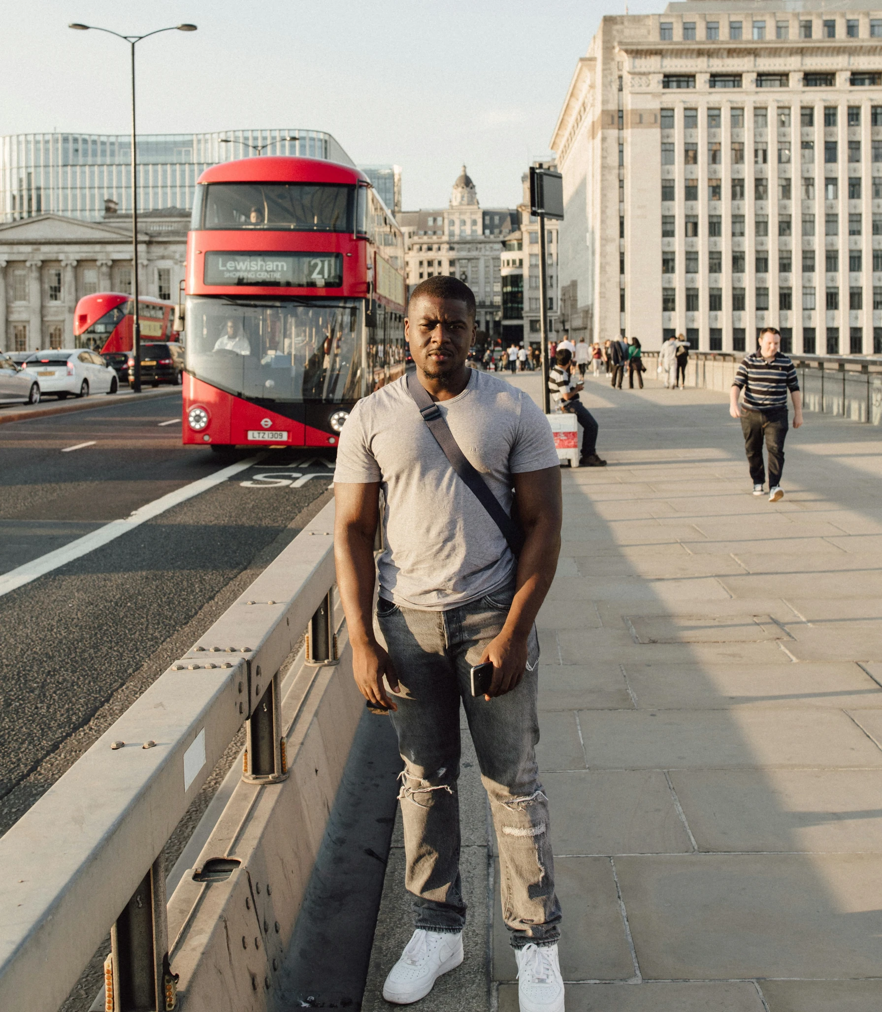 a man standing on a city sidewalk next to a red double decker bus