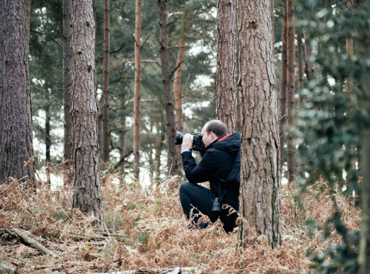a man sitting on a tree stump taking a po in the forest