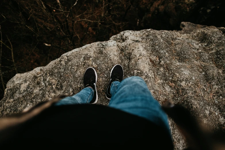 a pair of feet wearing blue jeans on a rock