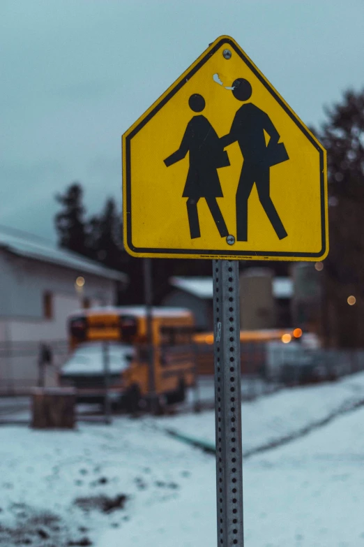 the street sign shows children crossing as snow surrounds a house