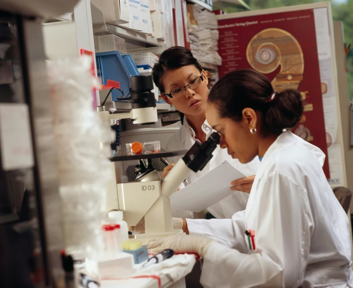 two people in lab coats looking through microscopes