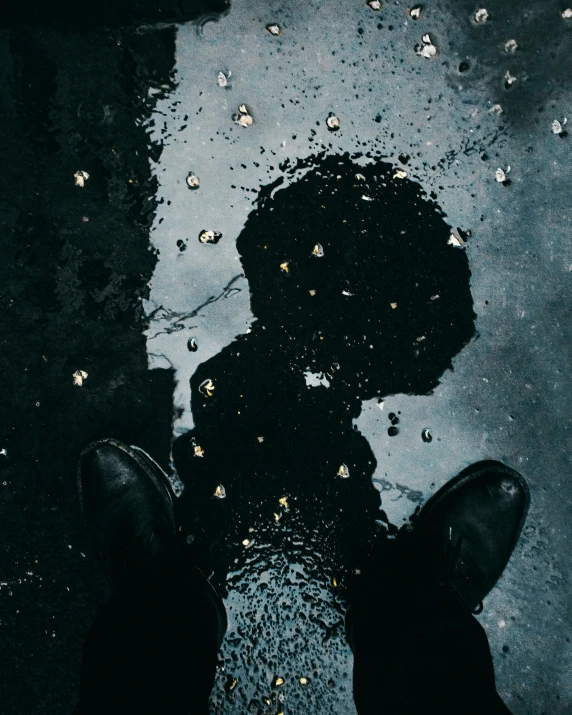 a man standing on a sidewalk underneath a wet umbrella