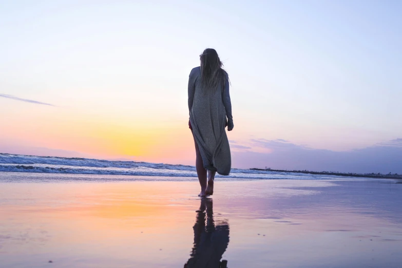 a woman walking along the beach holding a surfboard at sunset