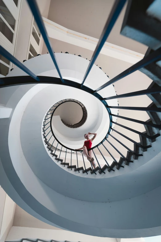 a woman in a red dress standing under a spiral staircase