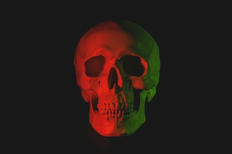 a red, green and black skull sitting on a dark surface