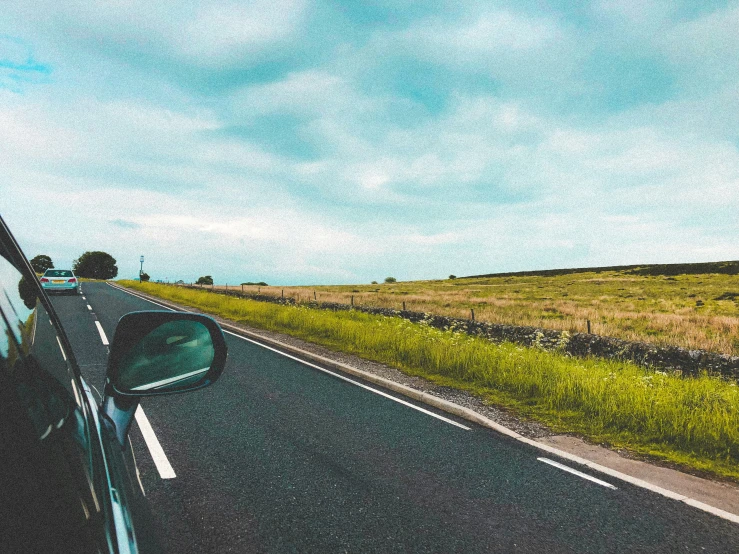 a car on a road traveling next to a lush green field