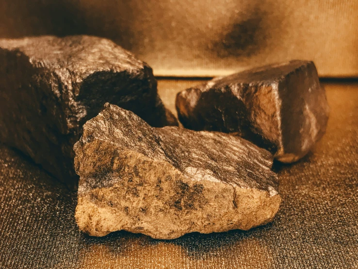 two rocks, one brown and the other black, are on a gold metallic surface