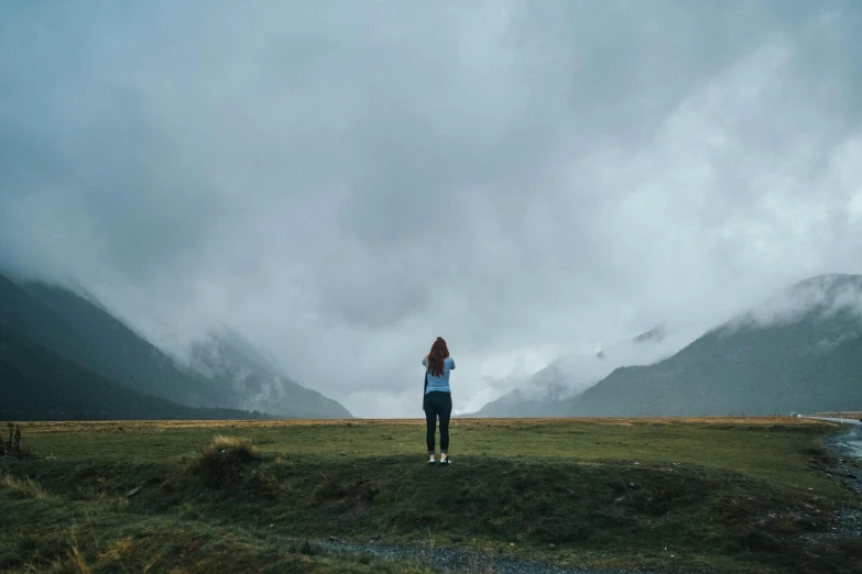 the woman in blue is standing on a hill and clouds