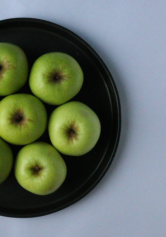 a bowl filled with green apples on top of a table