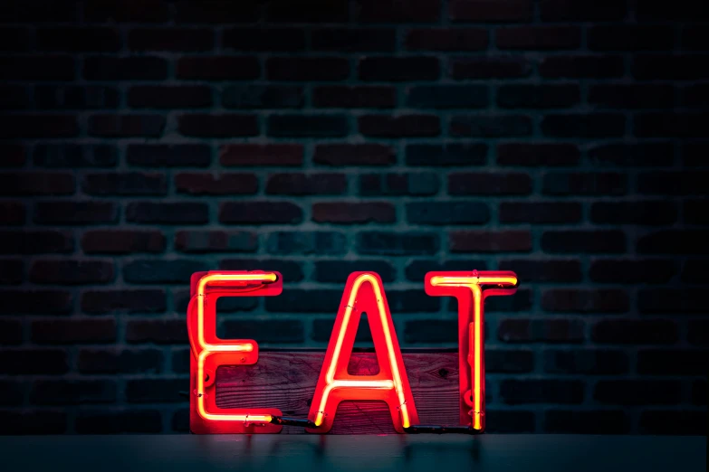 a neon sign reads eat on a table in front of a brick wall