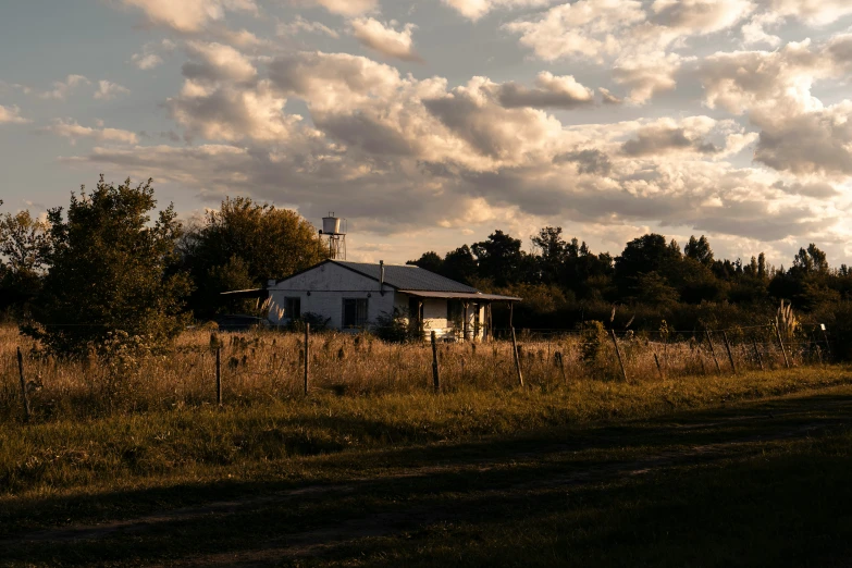 a house in a grassy field with trees and clouds