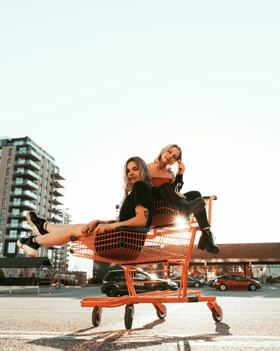 two women are riding on the back of an orange shopping cart