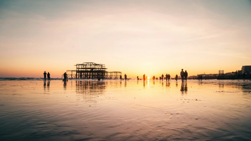 the sun is setting over the water and some people are standing on the beach