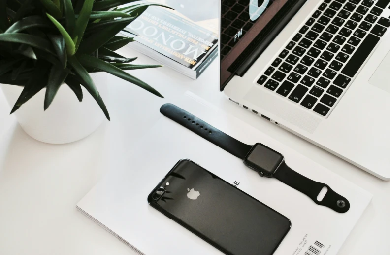 a close up of a cellphone on a desk with an iphone and a plant