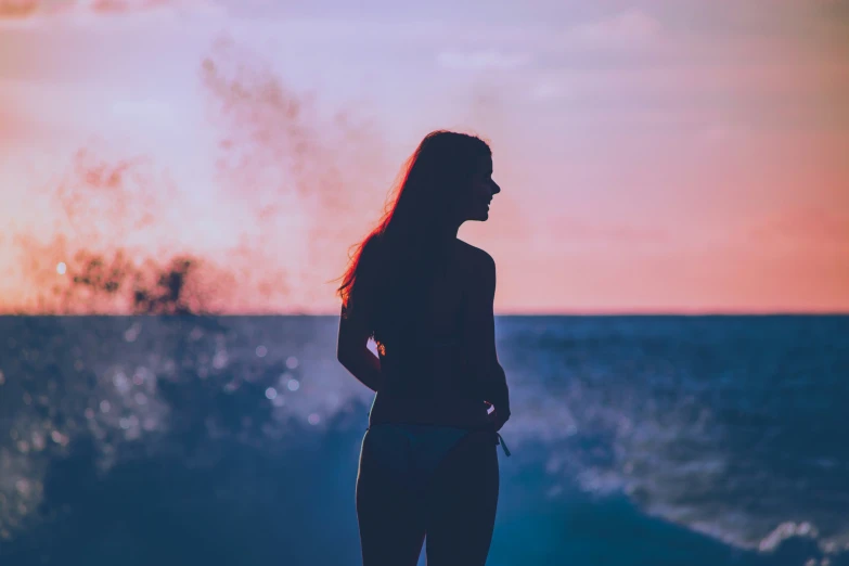 there is a woman standing on the beach at sunset