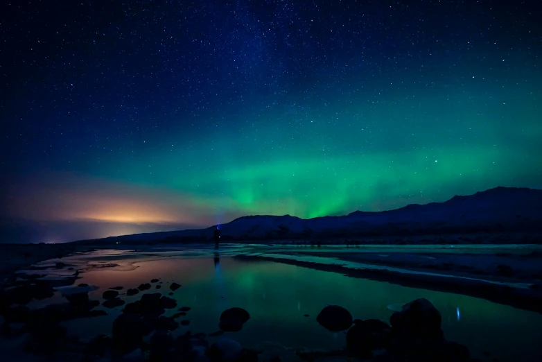 a starr filled night sky with the aurora over some mountains and water