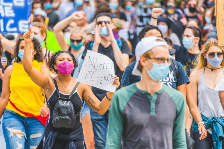 the crowd of people wearing face masks are holding signs