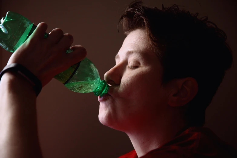 a woman drinking from a green bottle in the dark