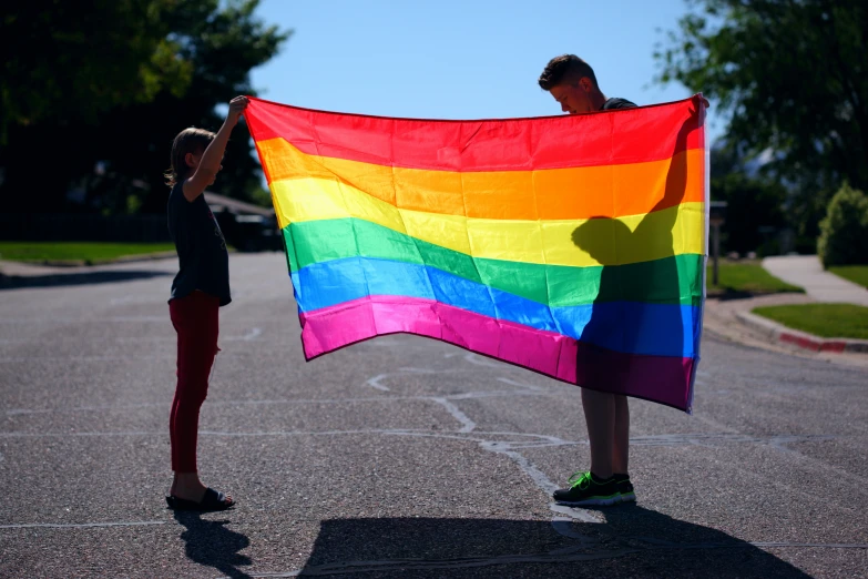 a man and woman standing in a parking lot holding a rainbow flag
