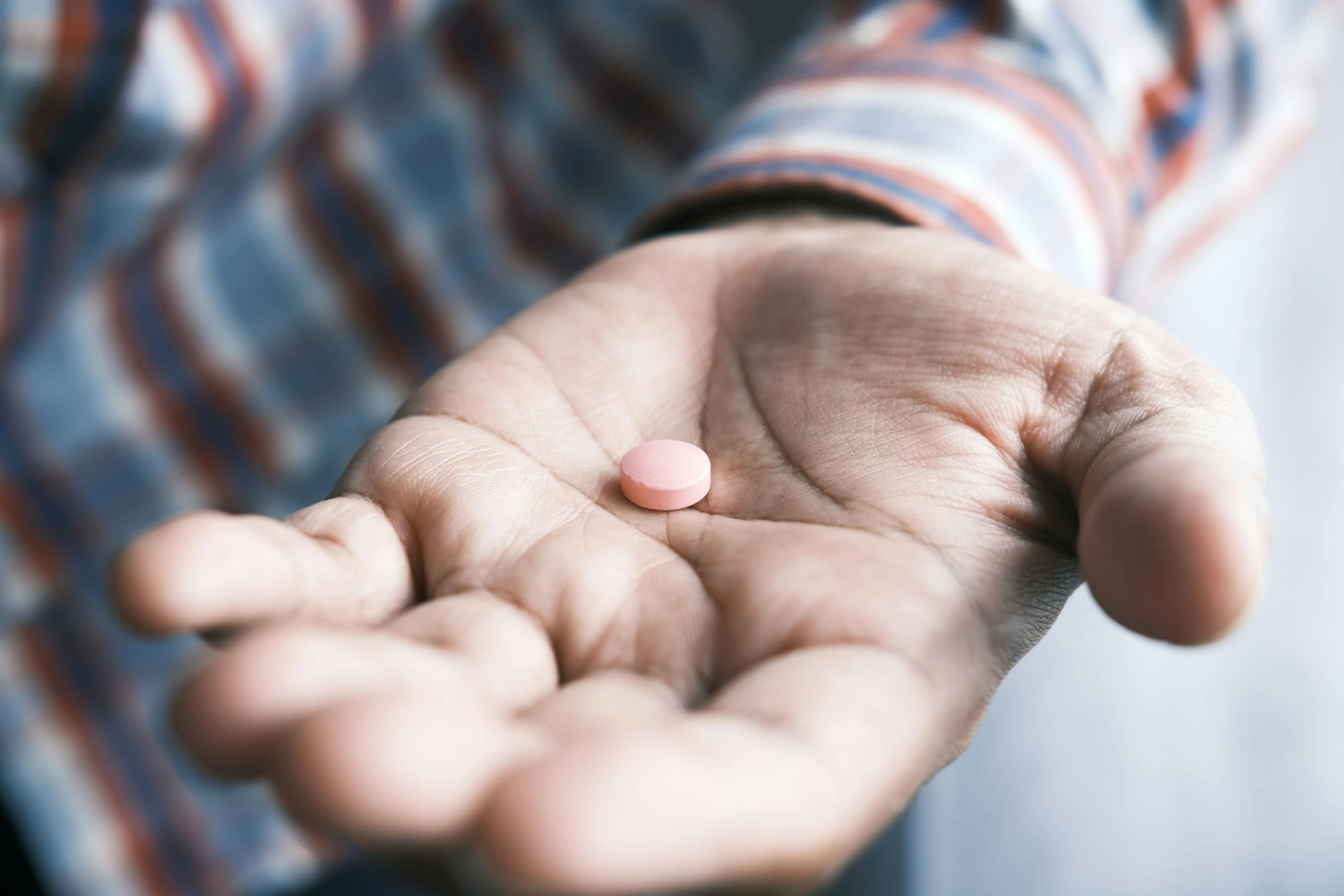 person holding their hand out and some pink pills in it