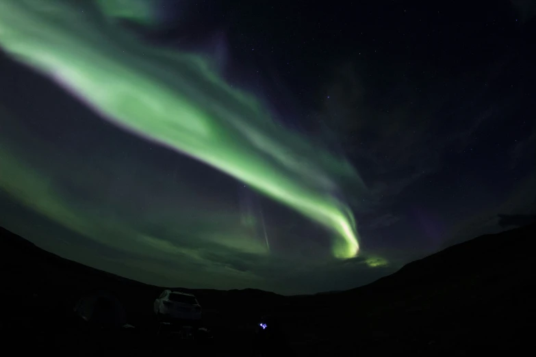 bright green light streams through the sky above the hills