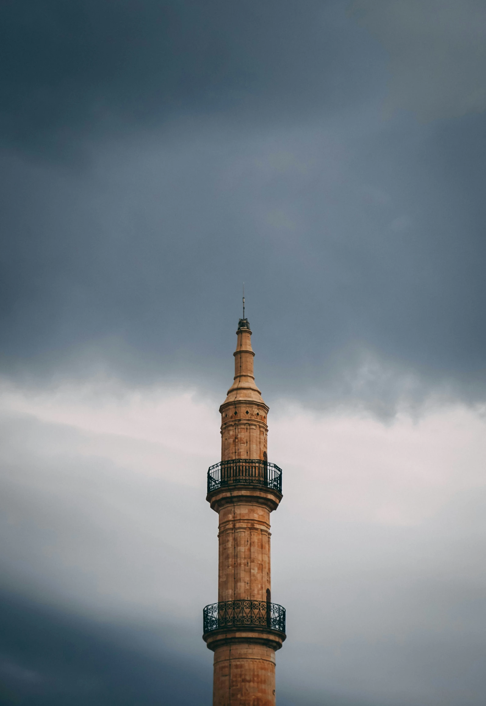 a tall tower sitting under dark clouds with a clock on it's side