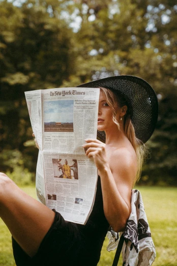 a woman in black hat holding a newspaper while sitting down
