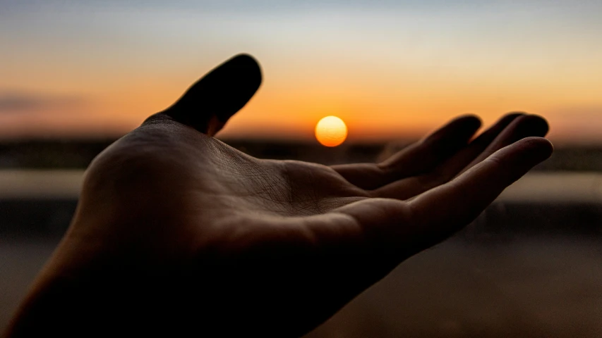 a hand reaching towards a sunset through its palm