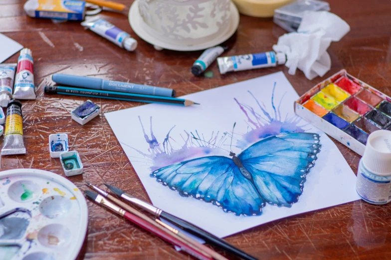 many colored paints, a cup of water and two erflies on the table