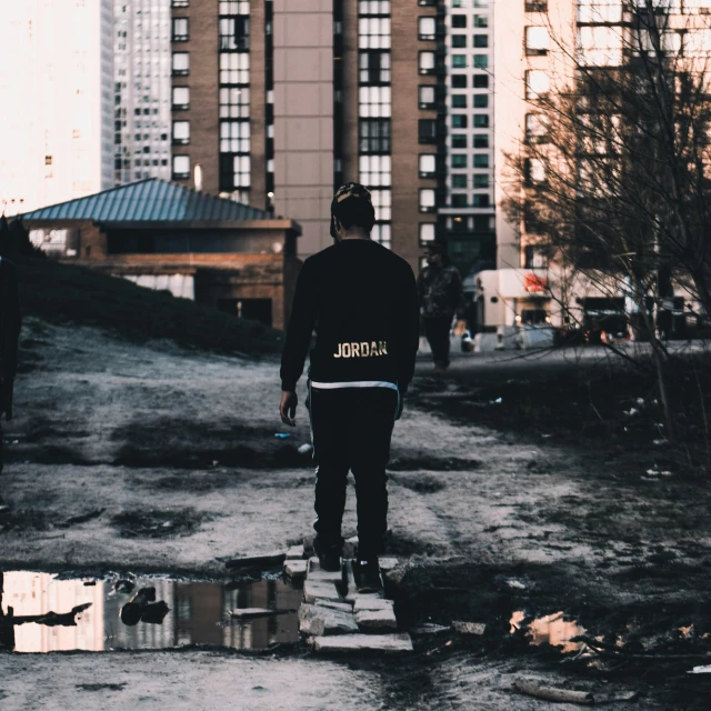 skateboarder wearing black jacket, holding two boxes near an urban area